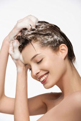 A female washing her hair with soapy water, smiling, great clear skin